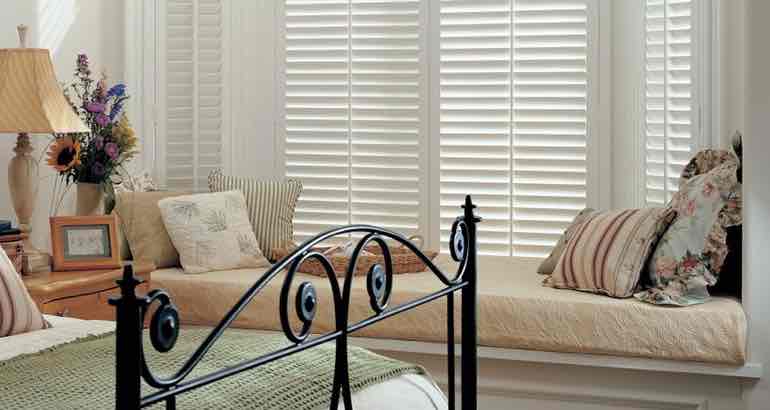 White shutters in a white bedroom bay window.